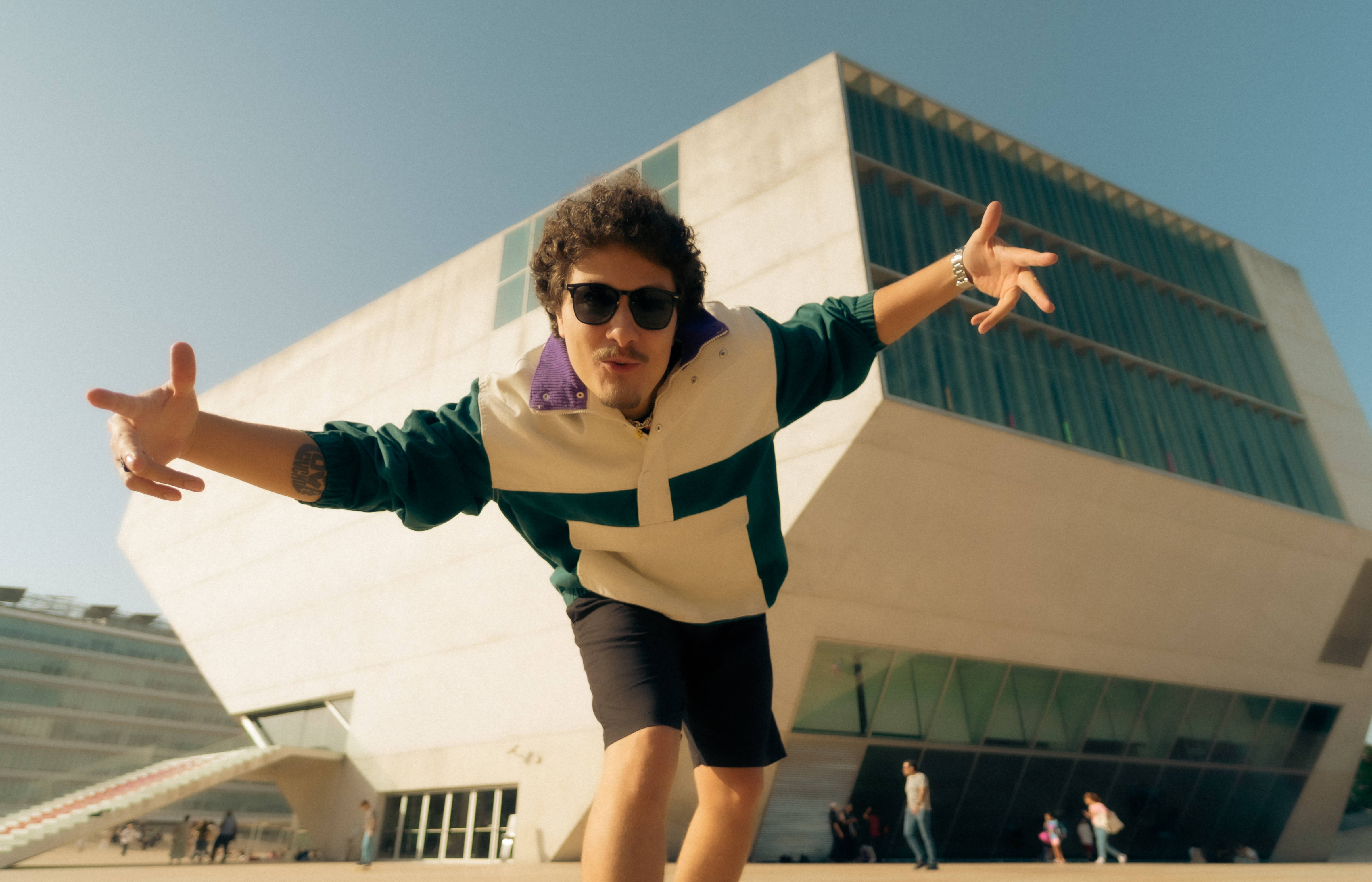 DJ Tilulu de braços abertos em frente a um prédio moderno