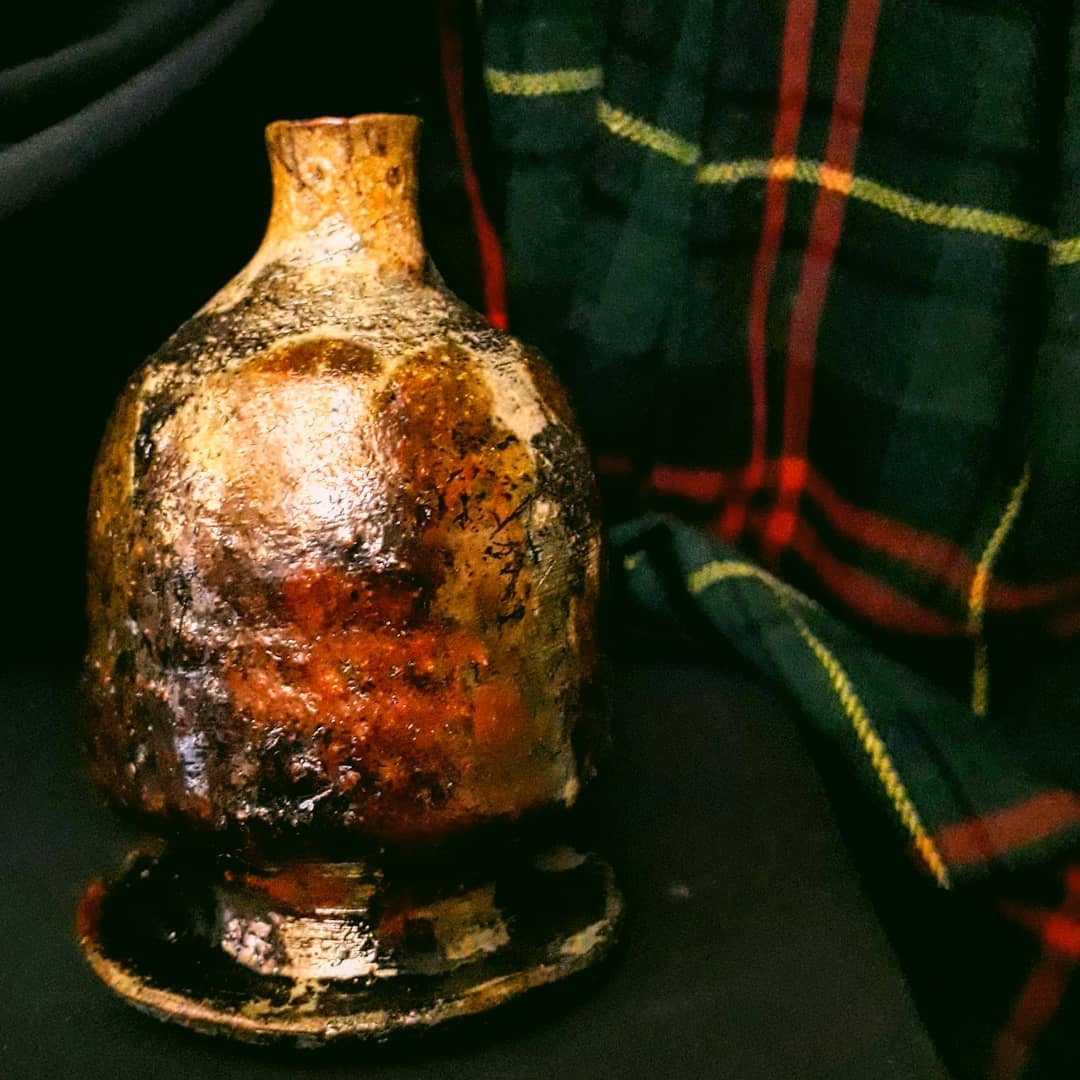 Garrafa de cerâmica com corpo irregular e gargalo estreito, esmalte marmorizado em marrom escuro, laranja queimado e dourado, com áreas carbonizadas de queima