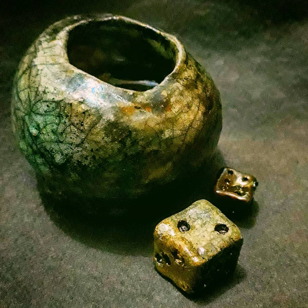 Vaso de cerâmica com esmalte craquelado em verde-oliva, musgo e bronze, de abertura ovalada assimétrica, ao lado de dois dados de cerâmica do mesmo acabamento