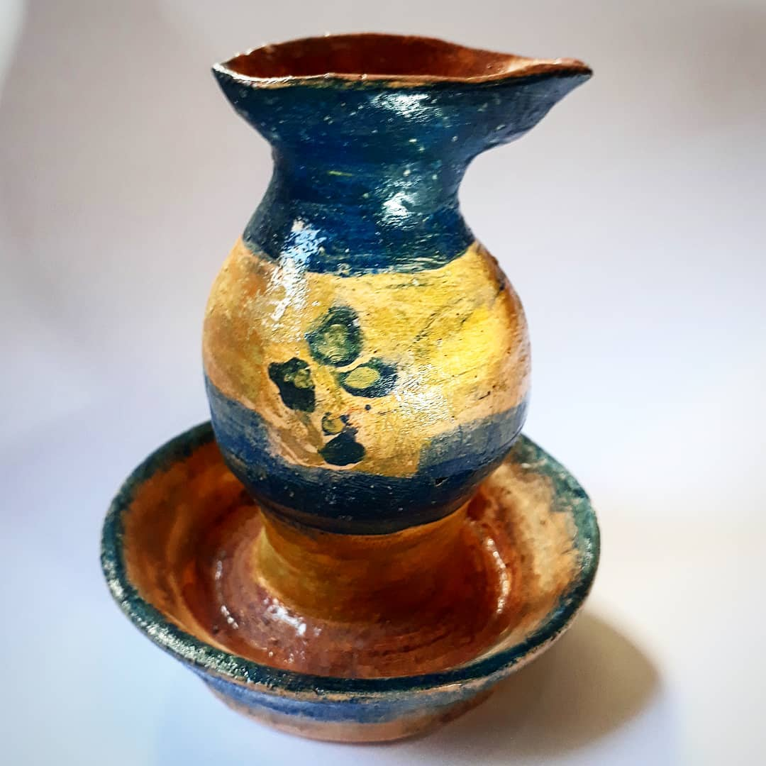 Conjunto de cerâmica com jarra de bico vertedor em azul escuro e amarelo-ocre, encaixada numa tigela rasa de interior em barro natural